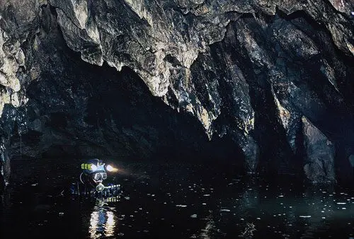 Person exploring a dark cave with water by kayak.
